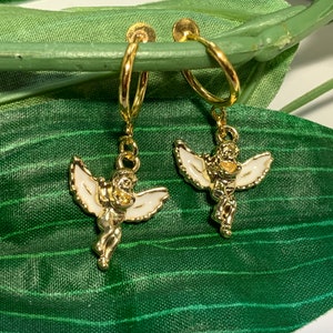 May include: A pair of gold hoop earrings with angel charms. The angels are white with gold accents and have wings.