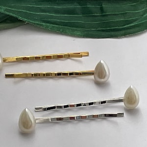 Op de afbeelding: Twee sets haarclips met parelmoerachtige, traanvormige accenten. De ene set is goud en de andere is zilver.