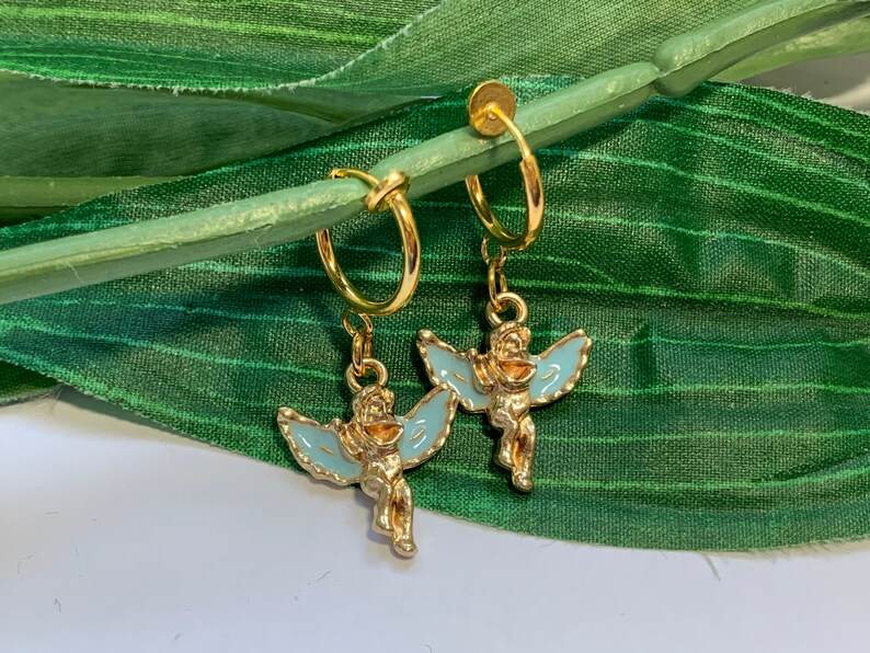 May include: A pair of gold hoop earrings with a blue enamel angel charm hanging from each hoop.