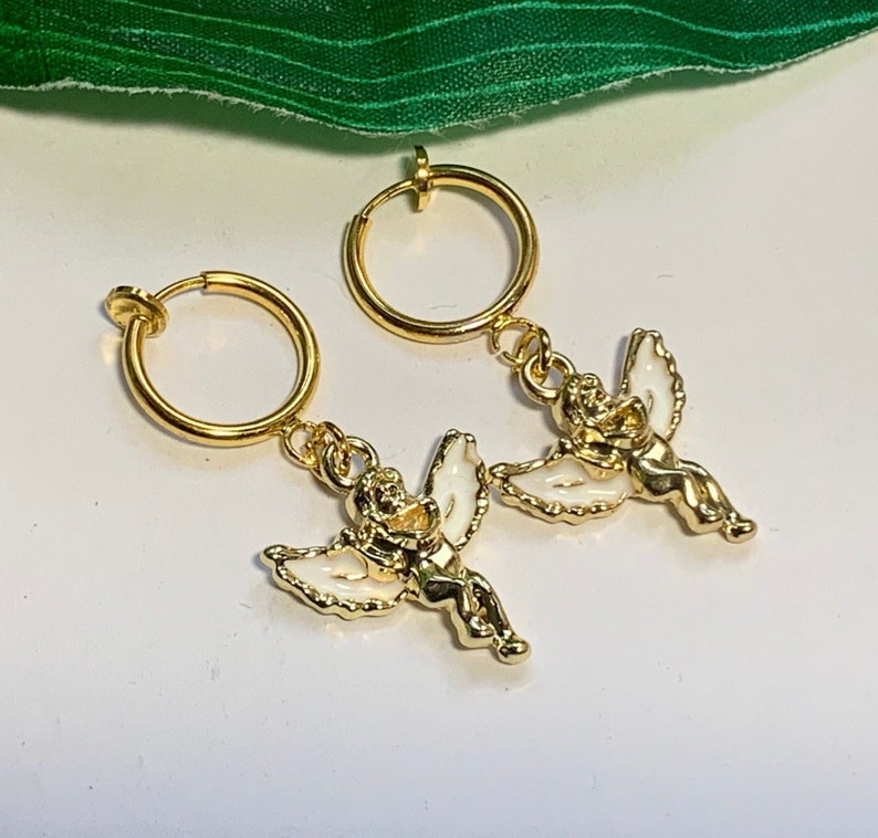 May include: A pair of gold clip-on earrings with a small angel charm hanging from each hoop.