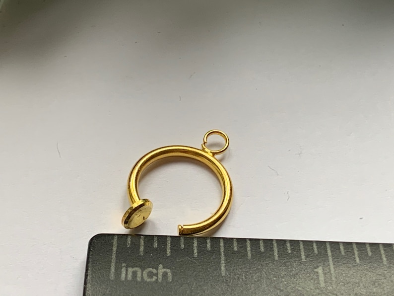 May include: A gold-colored metal ring with a small loop at the top. The ring is about 1 inch in diameter.