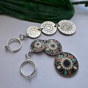 May include: A pair of silver clip-on earrings with colorful, patterned, round charms. The earrings have a simple, circular design and are perfect for adding a touch of bohemian style to any outfit.