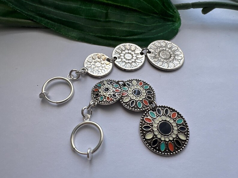 May include: A pair of silver clip-on earrings with colorful, patterned, round charms. The earrings have a simple, circular design and are perfect for adding a touch of bohemian style to any outfit.