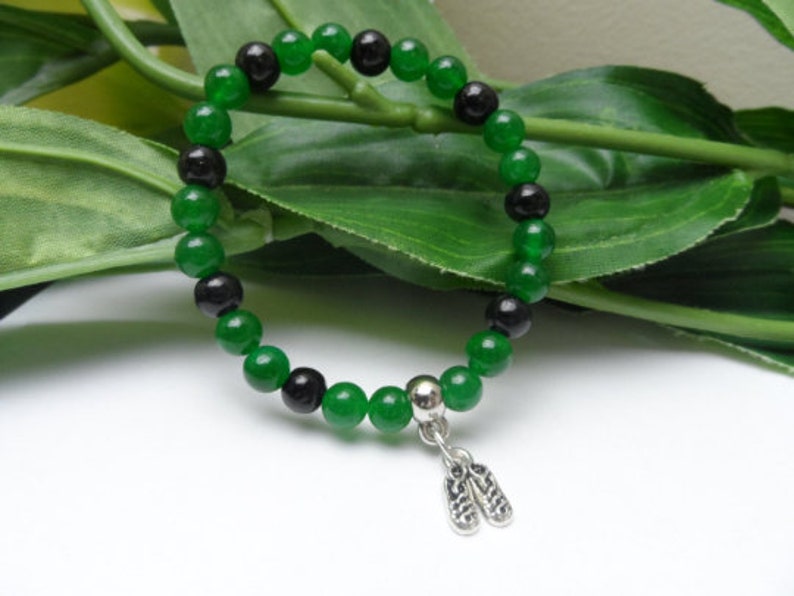 May include: A green and black beaded bracelet with a silver charm. The charm is shaped like a pair of flip flops.