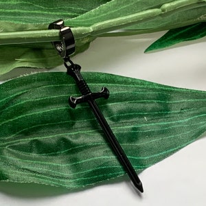 May include: Black sword earring with a hoop design. The sword is detailed with a cross guard and a pointed tip.