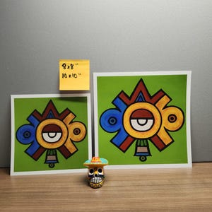 May include: Two colorful prints of a stylized geometric design with a red, yellow, blue, and green color scheme. The prints are on white paper with a green border. The smaller print is 8x8 inches and the larger print is 10x10 inches. A small, colorful, ceramic skull with a hat is in the foreground.