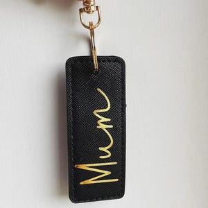May include: Black leather keychain with a gold metal ring and a gold inscription that reads "Mum".