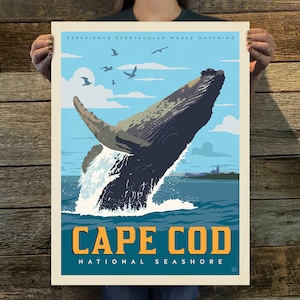May include: A vintage-style travel poster featuring a humpback whale breaching in the ocean. The poster has a blue background with white clouds and a lighthouse in the distance. The text "EXPERIENCE SPECTACULAR WHALE WATCHING CAPE COD NATIONAL SEASHORE" is printed in yellow and blue on the poster.