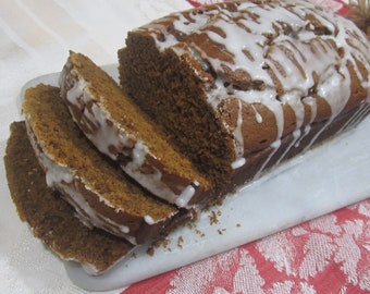 May include: A loaf of gingerbread bread with white icing, sliced and arranged on a white marble chopping board. The board is on a red and white tablecloth.