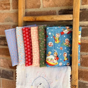 May include: A collection of six rectangular fabric pouches featuring various patterns, including a blue space-themed print with astronauts and rockets, a green floral print, a pink floral print, a red geometric print, and two light blue floral prints.