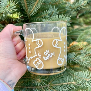 May include: A clear glass mug with a white gingerbread man design. The mug is filled with a brown liquid and has the text "Oh Snap!" on the front.