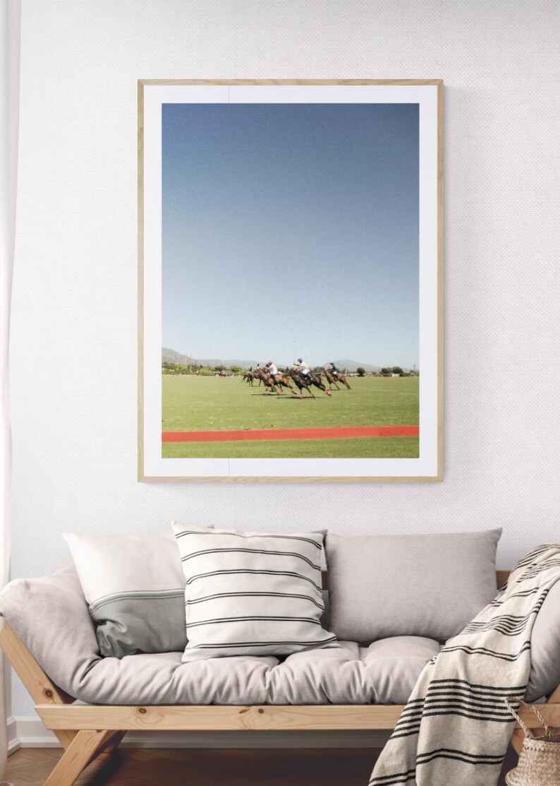 K&ouml;nnte beinhalten: Ein gerahmtes Foto eines Polospiels. Die Spieler reiten auf Pferden und befinden sich mitten im Spiel. Der Himmel ist blau und das Gras ist gr&uuml;n. Es gibt eine rote Linie auf dem Feld.