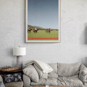 K&ouml;nnte beinhalten: Ein gerahmtes Foto eines Polospiels mit vier Reitern auf Pferden in einem Feld. Der Himmel ist blau und das Gras ist gr&uuml;n. Das Foto h&auml;ngt an einer wei&szlig;en Wand &uuml;ber einem grauen Sofa.