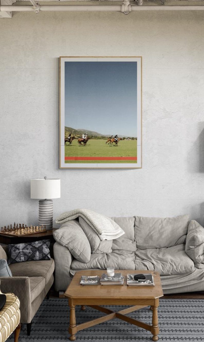 K&ouml;nnte beinhalten: Ein gerahmtes Foto eines Polospiels mit vier Reitern auf Pferden in einem Feld. Der Himmel ist blau und das Gras ist gr&uuml;n. Das Foto h&auml;ngt an einer wei&szlig;en Wand &uuml;ber einem grauen Sofa.