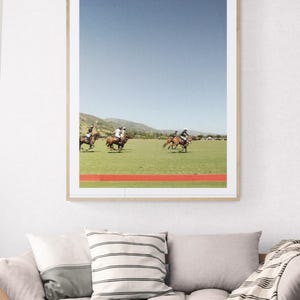 K&ouml;nnte beinhalten: Ein Foto von einem Polospiel mit vier Spielern auf Pferden, die &uuml;ber ein gr&uuml;nes Feld reiten. Die Spieler tragen wei&szlig;e Hemden und reiten braune Pferde. Der Himmel ist blau und im Hintergrund sind Berge zu sehen.