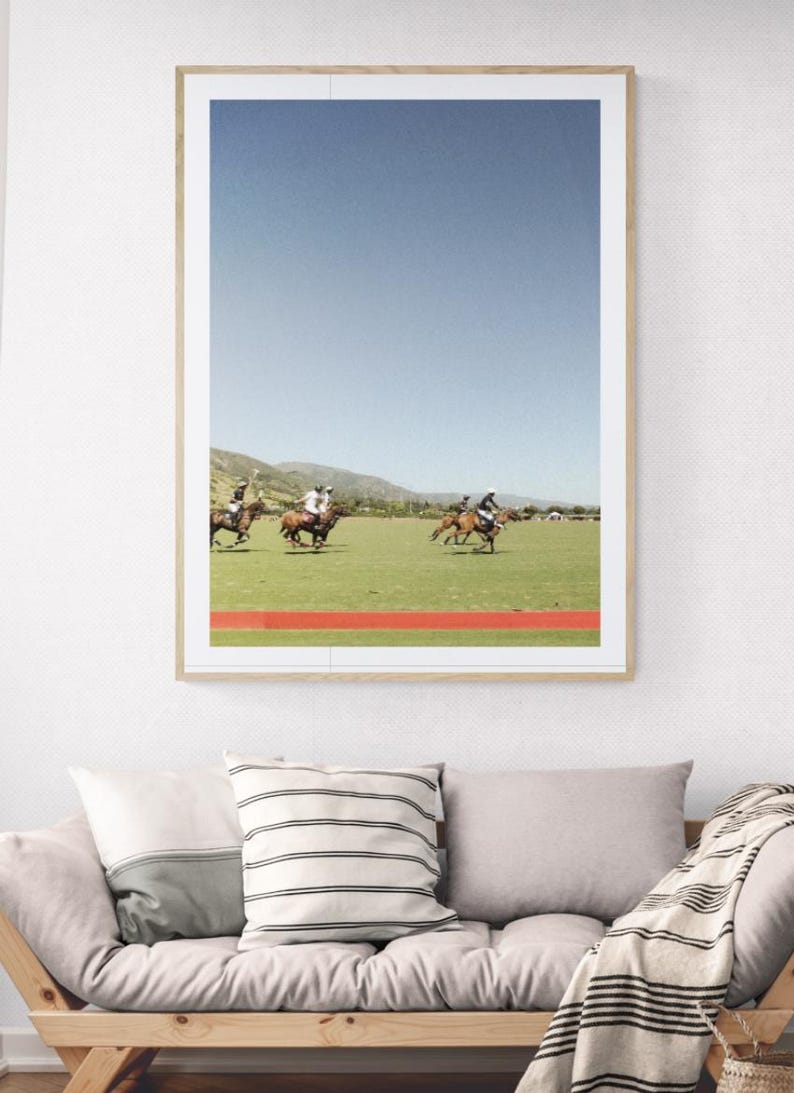 K&ouml;nnte beinhalten: Ein Foto von einem Polospiel mit vier Spielern auf Pferden, die &uuml;ber ein gr&uuml;nes Feld reiten. Die Spieler tragen wei&szlig;e Hemden und reiten braune Pferde. Der Himmel ist blau und im Hintergrund sind Berge zu sehen.