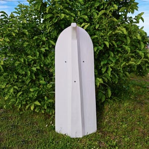 May include: A tall, white, vertical wooden structure with a rounded top and a central raised ridge running down its length. The object features three small, dark, circular fasteners or screws embedded along the central vertical spine.