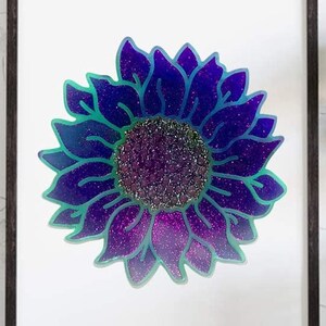 Puede incluir: Una impresión enmarcada de un girasol morado y azul con un centro brillante. El girasol está contorneado en un color turquesa.