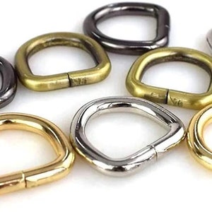 May include: Assortment of metal D-rings in various finishes, including gold, silver, and black. The rings are all the same size and shape, and they are perfect for attaching to bags, belts, or other accessories.
