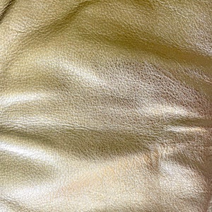 May include: Close-up of a textured, gold-colored leather surface. The leather has a subtle sheen and a slightly wrinkled appearance.