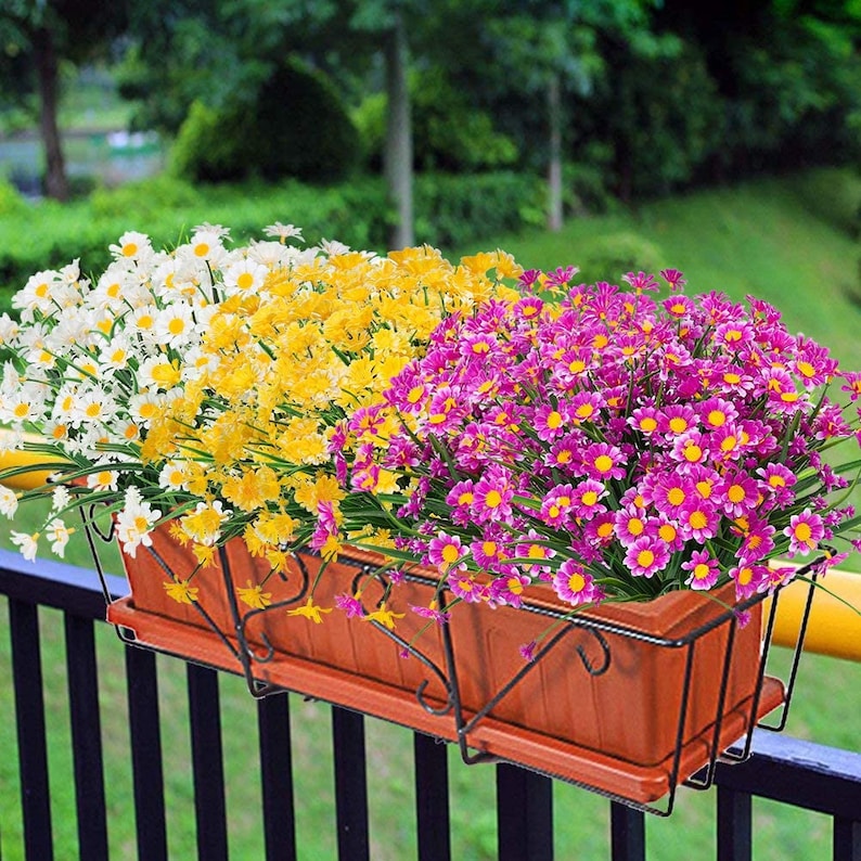 Pode incluir: Dois vasos marrons com suportes de metal preto est&atilde;o cheios de flores artificiais. O vaso &agrave; esquerda tem flores brancas e amarelas, enquanto o vaso &agrave; direita tem flores cor-de-rosa.