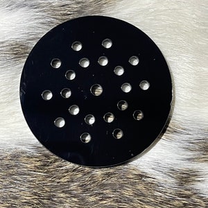May include: A black metal round disc with multiple small holes evenly spaced throughout the surface.