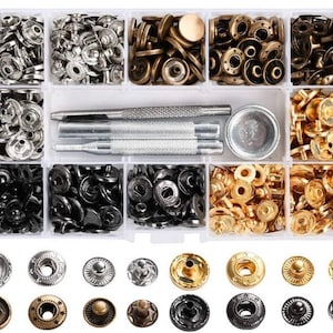 May include: A clear plastic storage box filled with various sizes and colors of metal snap fasteners. The box includes two metal tools for attaching the snaps.