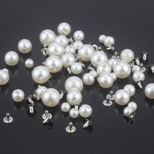 Può includere: Una collezione di bottoni di madreperla bianca con retro in metallo argentato. I bottoni sono sparsi su una superficie nera.