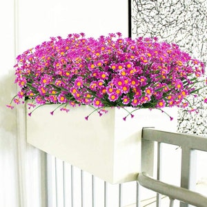 Pode incluir: Um vaso branco com uma grade atr&aacute;s, cheio de um grande buqu&ecirc; de flores artificiais cor-de-rosa.