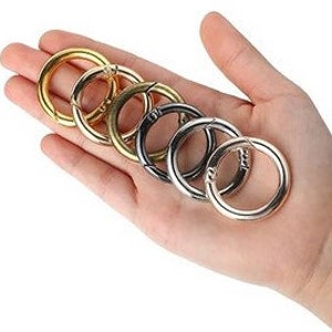 Könnte beinhalten: Sechs Schlüsselringe aus Metall in verschiedenen Farben, darunter Gold, Silber und Schwarz. Die Ringe sind offen und haben einen federbelasteten Mechanismus.
