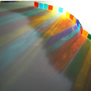Può includere: Una fila di quadrati di vetro colorati che proiettano luce arcobaleno su una superficie bianca.