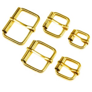 May include: Four gold-toned metal belt buckles of different sizes. The buckles are all rectangular with a rounded edge and a single prong.