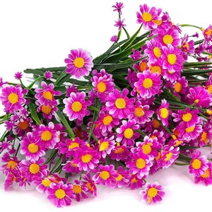 Pode incluir: Um ramo de flores de margarida artificiais cor-de-rosa com centros brancos. As flores est&atilde;o dispostas em um ramo e t&ecirc;m caules verdes.