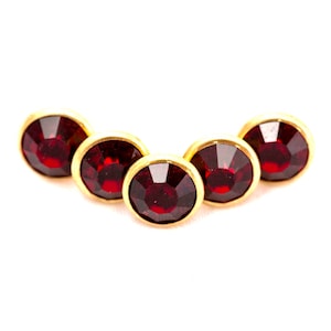 May include: Five red rhinestones set in gold settings, arranged in a slight arc.