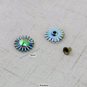 May include: Two iridescent rainbow colored metal flower-shaped buttons with a 15mm diameter. The buttons have a raised center and a flat back. A small metal stud is also included.