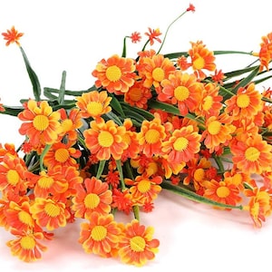 Pode incluir: Um ramo de flores de margarida artificiais laranja e amarelas com caules verdes.