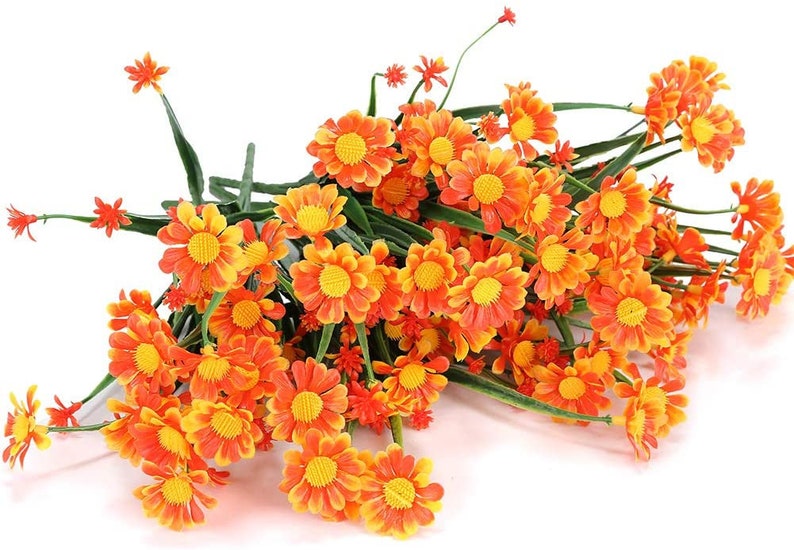 Pode incluir: Um ramo de flores de margarida artificiais laranja e amarelas com caules verdes.
