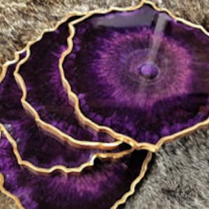 Puede incluir: Juego de cuatro posavasos de resina púrpura con ribete dorado. Cada posavasos tiene un patrón único de remolino.