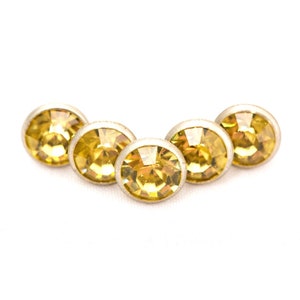 May include: Five gold-toned round rhinestones with clear yellow centers arranged in a slight arc.
