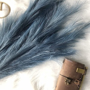 以下が含まれることがあります： 白いふわふわの表面に置かれた、青いドライパンプキン草の束。インテリアに人気です。