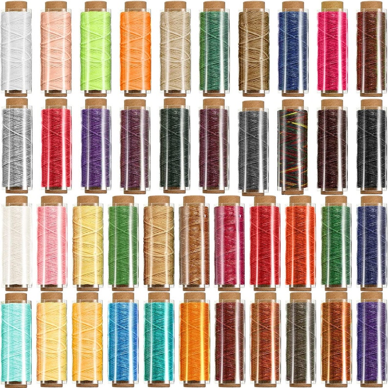 Puede incluir: Un conjunto de 48 carretes de hilo encerado en varios colores, incluyendo blanco, rosa, amarillo, verde, naranja, marr&oacute;n, azul, rojo, morado, negro y gris. Los carretes est&aacute;n dispuestos en filas y todos est&aacute;n en contenedores de pl&aacute;stico transparente con tapas marrones.