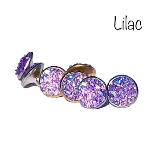 May include: Lilac colored glitter stud earrings. The earrings are round and have a silver backing.