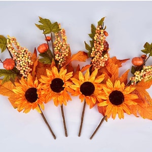 Könnte beinhalten: Ein Strauß künstlicher Sonnenblumen mit orangefarbenen und gelben Blütenblättern und braunen Zentren. Die Stiele sind mit kleinen, orangefarbenen Kürbissen und weißen Beerenbüscheln verziert.