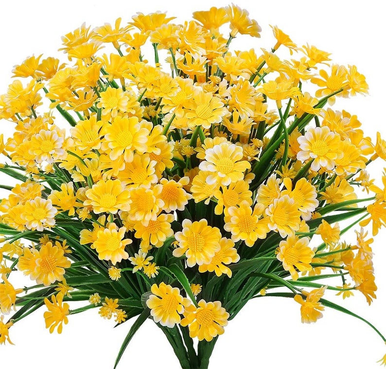 Pode incluir: Um buqu&ecirc; de flores de margarida amarelas artificiais com caules e folhas verdes. As flores est&atilde;o dispostas em um cacho, com algumas das flores voltadas para a c&acirc;mera e outras voltadas para fora.