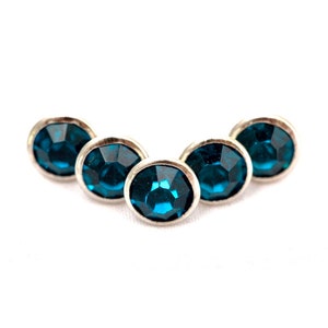 May include: Five small, round, blue rhinestones set in silver metal settings. The rhinestones are arranged in a slight arc.