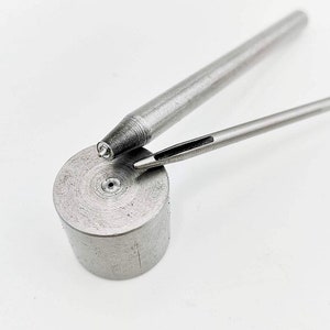 May include: Two metal tools for leather crafting. One tool is a long, thin, pointed awl with a handle. The other tool is a round, cylindrical punch with a small hole in the center.