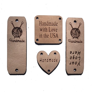 Puede incluir: Cuatro etiquetas de cuero marrón con diferentes diseños. La primera etiqueta es rectangular y dice "Handmade" con una bola de hilo y agujas de tejer. La segunda etiqueta es rectangular y dice "Handmade with Love in the USA". La tercera etiqueta es en forma de corazón y dice "Handmade". La cuarta etiqueta es rectangular y dice "Your Logo Here".