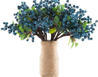 May include: A decorative floral arrangement featuring teal-colored berry clusters and green leaves. The berries are arranged in a vase wrapped with natural twine. The stems are brown, and the background is white.