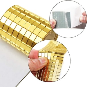 May include: Gold self-adhesive mosaic tiles on a roll. The tiles are small squares with a mirrored finish. The roll is shown with the adhesive backing exposed.
