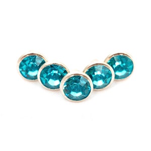 May include: Five turquoise blue rhinestones set in silver settings arranged in a slight arc.